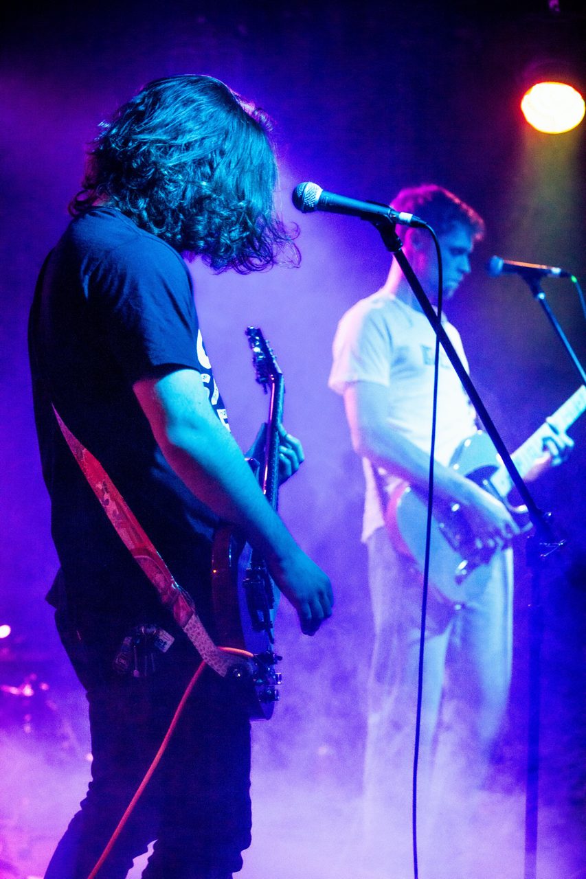 Two guitarists on stage under purple light