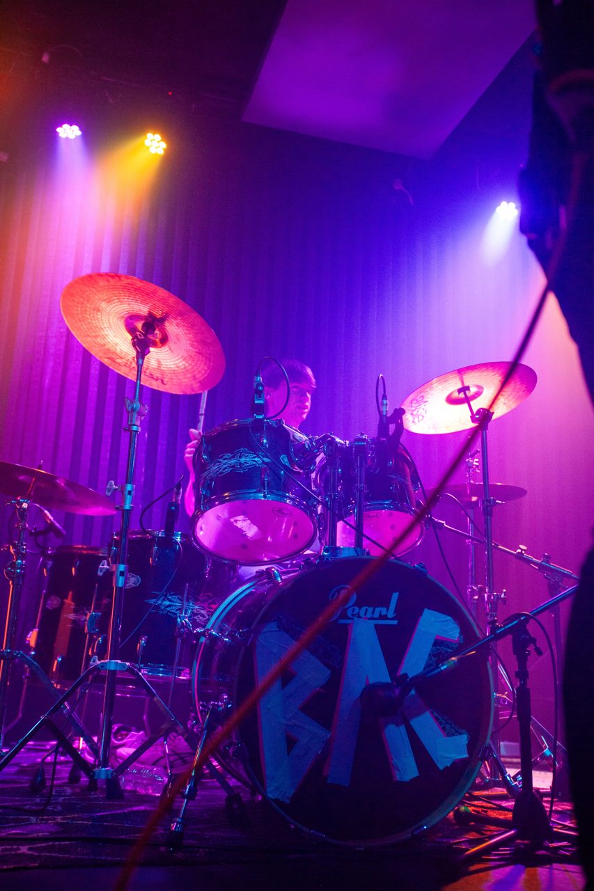 Drummer behind the BAC bass drum in purple stage light