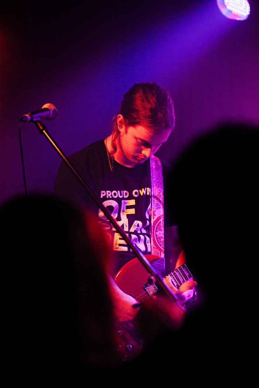 Guitarist playing a red guitar under magenta light