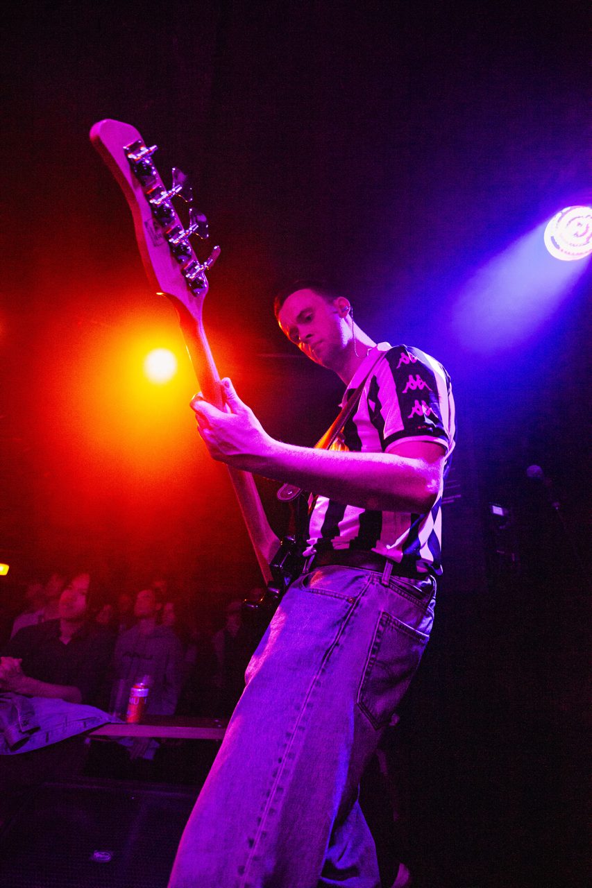 Bassist mid-riff with orange and blue stage lights